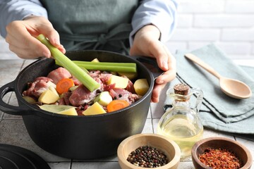 Woman preparing stew with vegetables and meat at white tiled table, closeup