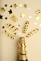 Confetti and bottle of sparkling wine on beige background, flat lay. Christmas decor