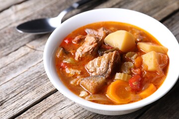 Delicious stew with vegetables in bowl and spoon on wooden table, closeup