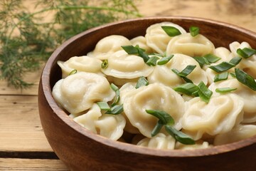 Delicious pelmeni with green onion in bowl on wooden table, closeup