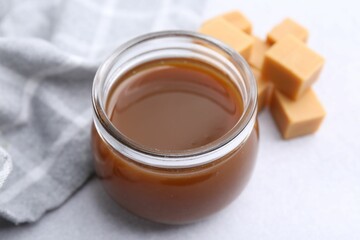 Tasty caramel sauce in jar and candies on light table, closeup