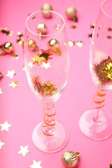 Wine glasses with confetti on pink background, closeup. Christmas decor