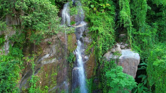 Aerial shot from up to down of the Huai Tueng Thao waterfall flowing down a high rocky cliff, Thailand