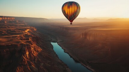 Obraz premium A vibrant hot air balloon hovers peacefully above a stunning canyon, reflecting the warm hues of dawn as the river winds below. The tranquility captures the beauty of early morning adventures