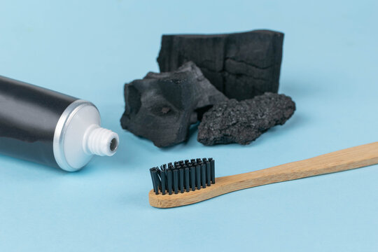 Charcoal Toothpaste and Bamboo Toothbrush with Activated Charcoal Pieces on Blue Background