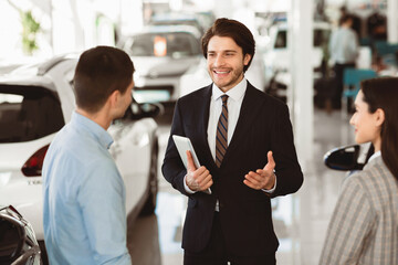 Car Sales Business. Auto dealer talking with couple clients, selling automobile, holding digital tablet. Selective focus
