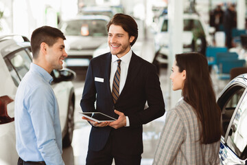 Discussing The Purchase. Young Family Speaking With Professional Car Seller In Dealership Center