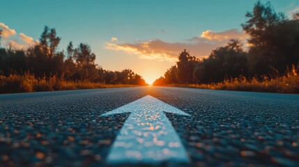 Low angle photography of a white arrow on the asphalt road during the sunset. Straight ahead way concept, path to success direction, business career future guidance, journey to the destination