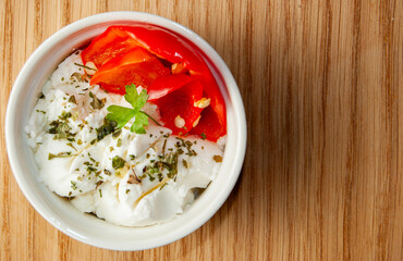 Fresh white cheese served in a small white bowl, accompanied by fresh peppers and parsley. 