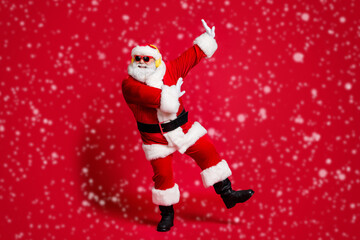 Feel young again. Full length photo of retired old man grey beard raise hands partying have fun wear santa costume sunglass headwear leather black boots isolated red color background
