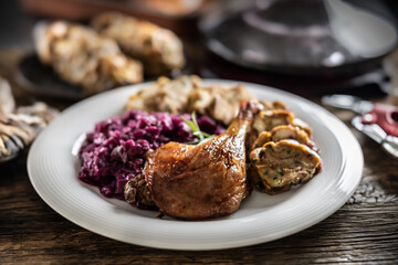 Portion of roast duck leg red cabbage homemade dumplings on plate and red wine on the background
