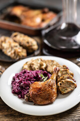 Portion of roast duck leg red cabbage homemade dumplings on plate and red wine on the background