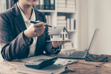 Real Estate Agent Presenting House Model: A professional realtor in a sleek suit confidently...