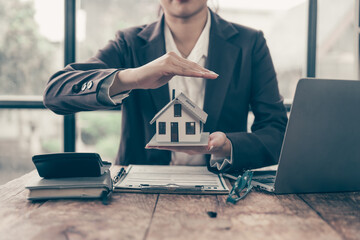 Securing Your Dream Home: A real estate agent's protective hands cradle a miniature house,...