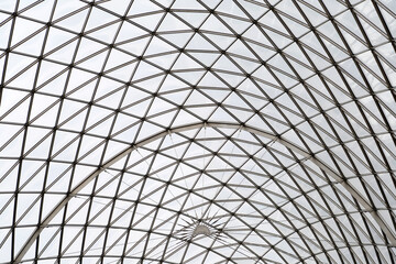 Vast ceiling showcases a stunning geometric design, blending glass and metal in an elegant framework, inviting natural light into an expansive area below