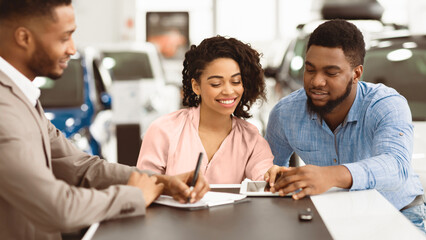 Buying Car. African American Spouses Signing Papers With Auto Seller In Dealership Office. Selective Focus, Panorama