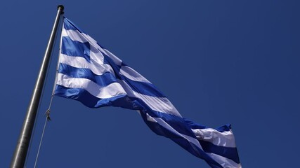 Greek flag waving on flagpole with blue sky in background