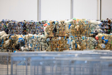 This image shows large bundles of compressed recycled plastic materials, stacked in a warehouse or recycling facility. 