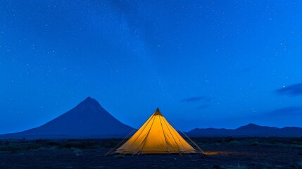 A yellow tent stands under a starry sky in a Kamchatka campsite. The silhouette of Vilyuchik volcano, shaped like a cone, rises in the dark blue night.