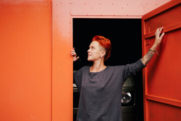 Woman with vivid hair opening garage door near camper van