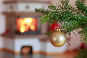 Christmas ball on fir tree branch and blur burning fireplace background.