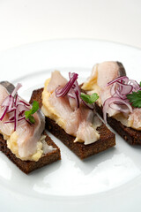 Open-faced sandwiches with herring and onions served on a white plate