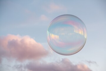 A large, iridescent soap bubble floats against a pastel-colored sky with soft clouds.
