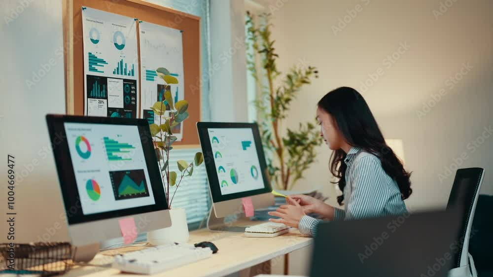Poster Businesswoman is analyzing financial data displayed on computer monitors and a wall-mounted board, using sticky notes for reminders and brainstorming