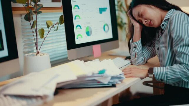 Young accountant feels overwhelmed by paperwork and pressure, staring at a computer screen filled with charts and reports, struggling with stress and fatigue in a busy office environment