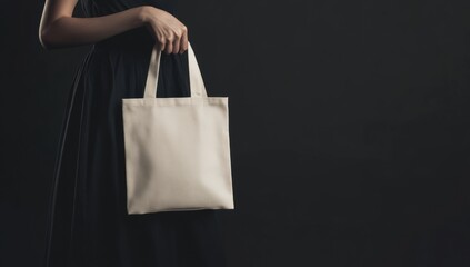 A woman holding a simple beige tote bag in a dark setting