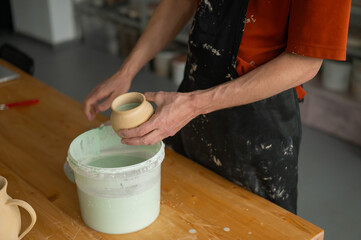 Close-up of a potter's hands glazing a pottery piece. 