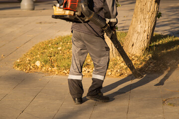 A man, a utility worker, removes leaves from the road with a special device.