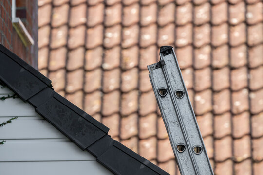 Metal extension ladder with several rungs leaning against side of a tiled house roof