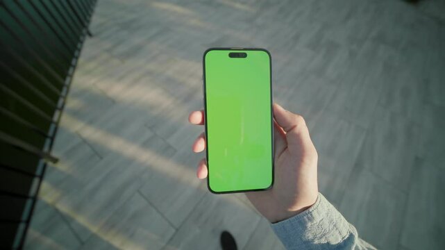 Hand holding and scrolling vertically phone with green screen moving around. On background lake. Typing on smartphone