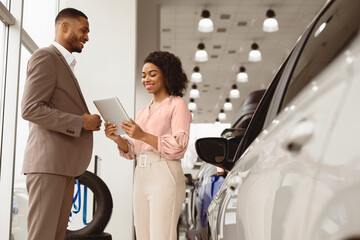 Car Sales. Automobile Seller Woman Showing Auto To African Businessman Standing In Dealership...