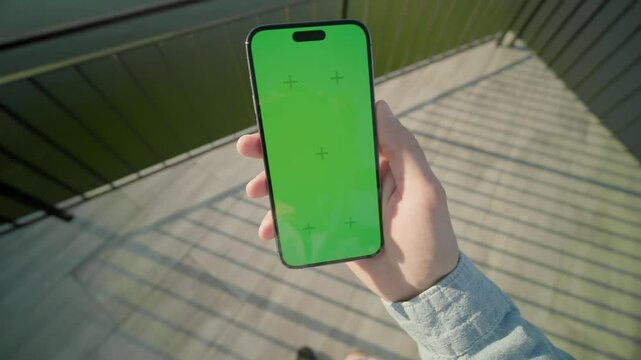 Shot of man hands holding vertically phone with green screen walking. On background beautiful lake. Nature. Typing on smartphone