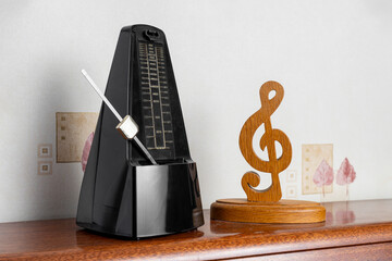 Traditional black metronome next to wooden treble clef on top of an upright piano