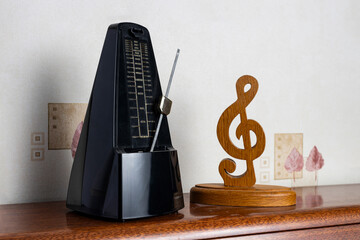 Traditional black metronome next to wooden treble clef on top of an upright piano