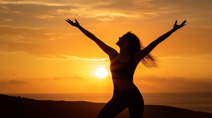 Fototapeta premium A woman stands on a hilltop, arms raised victoriously, silhouetted by a stunning sunset over the ocean. The warm glow envelops her, highlighting nature's beauty
