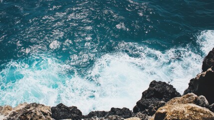 Obraz premium Bright sunlight illuminates the turquoise waves crashing against the rugged rocks of the coastline, creating a serene and picturesque ocean view