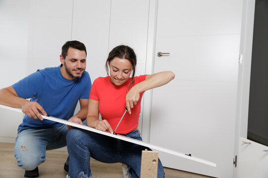 Young couple just married assembling a piece of furniture in their home. With screwdriver and tools in hand to follow the instruction book. Handyman couple. They are the owner.New house, new furniture