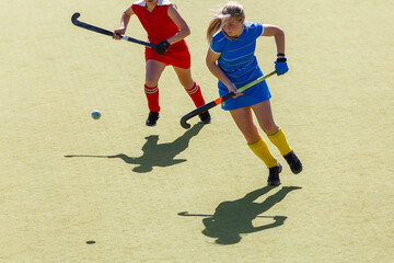 Two female field hockey players fighting for the ball on the pitch