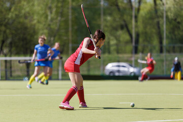 Female attacker hitting the ball in an intense field hockey match on a sunny afternoon