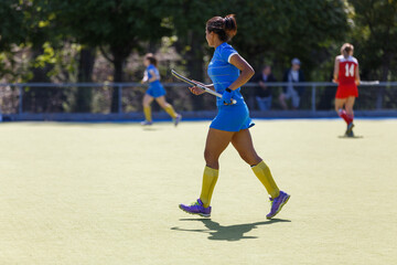 Young black field hockey player running with the stick on the turf