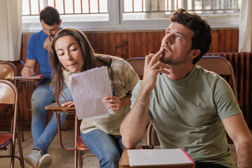 Obraz premium Group of students in class with their notes. Taking an exam, some try to look at the others'. If there are any doubts, they raise their hand and the teacher will help them. Concentration, university.