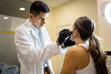 Obraz premium A Latino doctor in his 40s is consulting at a beauty center.The doctor is pointing to a woman's face with a pencil to know where she has to operate.Concept of Latino Hispanic Doctors.