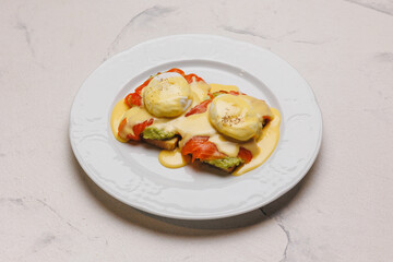 A hearty brunch of toast, avocado, salmon and poached eggs with cheese sauce.