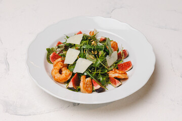 Hearty salad with shrimp and figs in a large white plate.