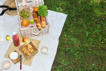 Picnic wicker baskets with delicious food, tableware and drink on white blanket outdoors, above view. Space for text