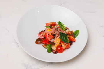 Appetizing salad with tomatoes, onions, olives and crispy croutons in a large white plate.